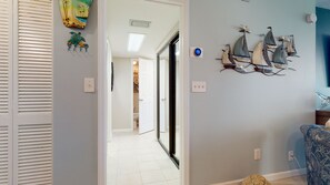 A hallway with a door leading to a room, a wall with decorative sailboat models, and a patterned chair.