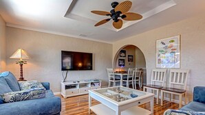 Un salon équipé d’un téléviseur, d’un ventilateur de plafond, d’un coin repas avec des chaises et d’une table basse.
