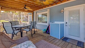 Une terrasse couverte avec une table et des chaises, un ventilateur de plafond et une porte avec une fenêtre.