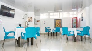 A dining area with blue chairs and white tablecloths, a television mounted on the wall, and a Coca-Cola refrigerator. - Hotel Tupinamba Neiva (Neiva)
