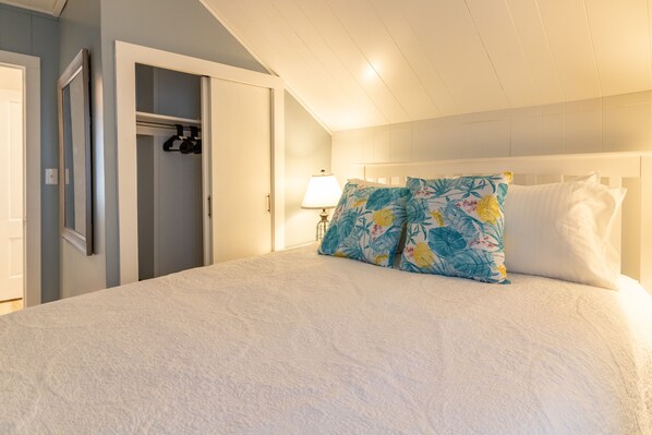 Une chambre à coucher avec un grand lit, une table de chevet avec une lampe, une armoire et une porte donnant sur une autre pièce.