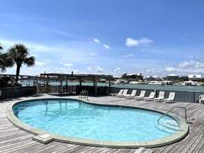 Una piscina con muelle de madera, sillas de descanso y vista hacia un muelle y edificios al otro lado del agua.