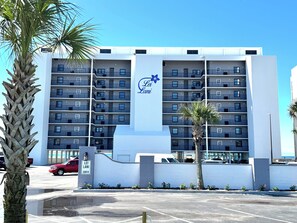 Un hotel de varios pisos con un llamativo letrero 'Lei Lai', un estacionamiento y una palmera en primer plano.