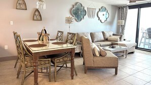 Un área de comedor con una mesa y sillas de vidrio, un sofá y decoración en la pared.