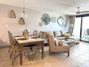 A dining area with a glass table and chairs, a sofa, and decorative wall art. - Lei Lani 504 2 King Beds  2 bedroom / 2 bath condo Amazing View (Orange Beach)
