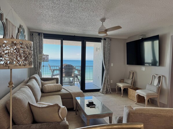 Una sala de estar con sofá, sillones, una mesa de centro, televisor y vista al océano.