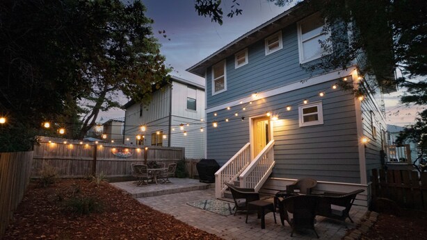 A backyard patio with a covered seating area, a barbecue grill, and string lights.
