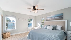 A bedroom with a bed, a ceiling fan, a window, and a painting on the wall.