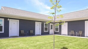 Un bâtiment dont les portes sont numérotées, un petit arbre au centre et une pelouse bien entretenue.