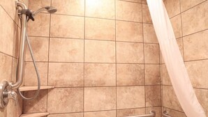 Un espace douche avec des murs carrelés, une douchette à main, un panneau de commande de la douche et une barre d’appui.