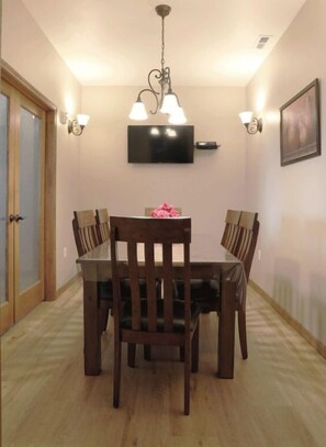 A dining area with a wooden table and chairs, a chandelier, wall-mounted lights, and a television on the wall.