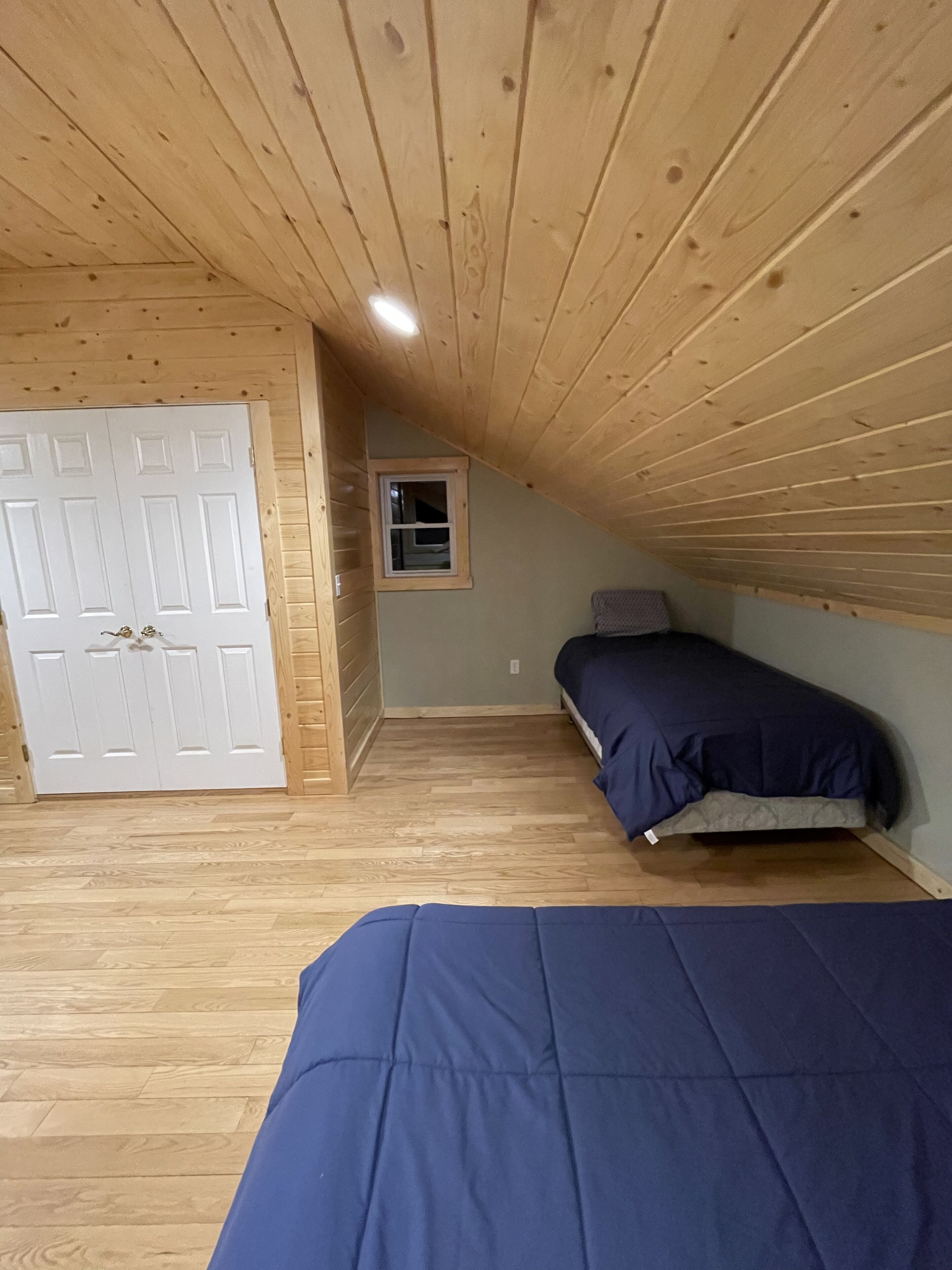 Un dormitorio con techo inclinado, paredes de madera, una ventana y una cama con ropa de cama azul.
