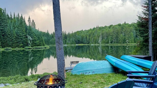 Un espace de détente aménagé au bord du lac, avec des fauteuils Adirondack, un foyer et un bateau abrité.