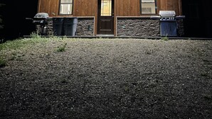 Une maison en bois avec une porte brun foncé, deux fenêtres et des fondations en pierre.