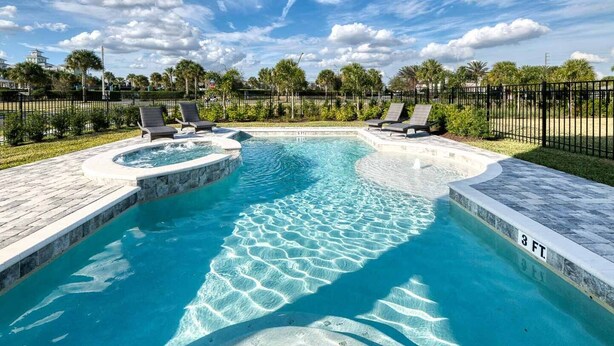 Une piscine avec un jacuzzi, entourée de chaises longues et de palmiers.
