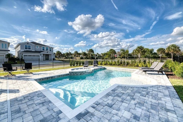 Une piscine bordée de pierres, des chaises longues et une terrasse dallée.