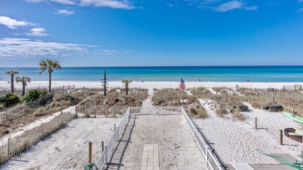 Ein Sandstrand mit einer Holzlattenzaun, einem wolkenlosen, tiefblauen Himmel und einer amerikanischen Flagge.