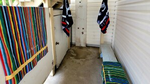A narrow hallway with a concrete floor, white walls, and a sloped ceiling. There are colorful striped blankets hanging on the wall and a bench with blankets on it. - Sunsplash 5, walk to beach, walk to Main Street (North Myrtle Beach)
