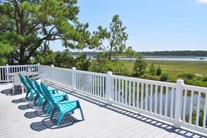 Een terras met turquoise stoelen en een witte reling, uitkijkend op een meer.