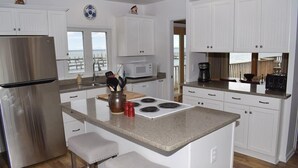 Una cocina moderna con armarios blancos, un refrigerador de acero inoxidable, un microondas y una estufa. Hay dos taburetes de bar y una cafetera en la encimera.