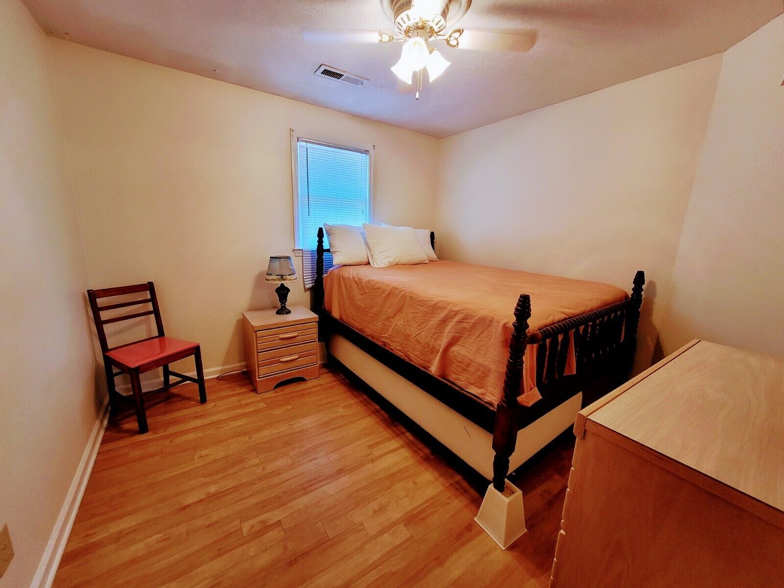 A bedroom with a wooden bed, a nightstand, a chair, and a window with blinds.