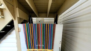 Un espacio de almacenamiento con una puerta blanca, una cortina a rayas de colores y una manta a rayas verdes y azules sobre un banco.