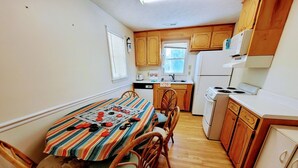 Una cocina compacta con armarios de madera, una mesa de comedor con sillas y un refrigerador.