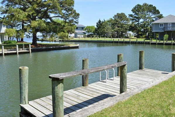Un muelle de madera se extiende sobre aguas tranquilas, rodeado de zonas verdes y árboles.