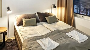 A neatly made bed with pillows and a blanket, a bedside table with a lamp, and a window with curtains.