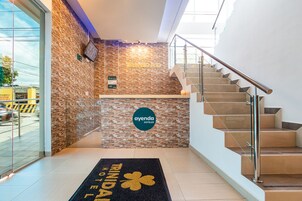 Zona de recepción de un hotel con pared de piedra, una escalera y puerta de cristal que da al exterior.