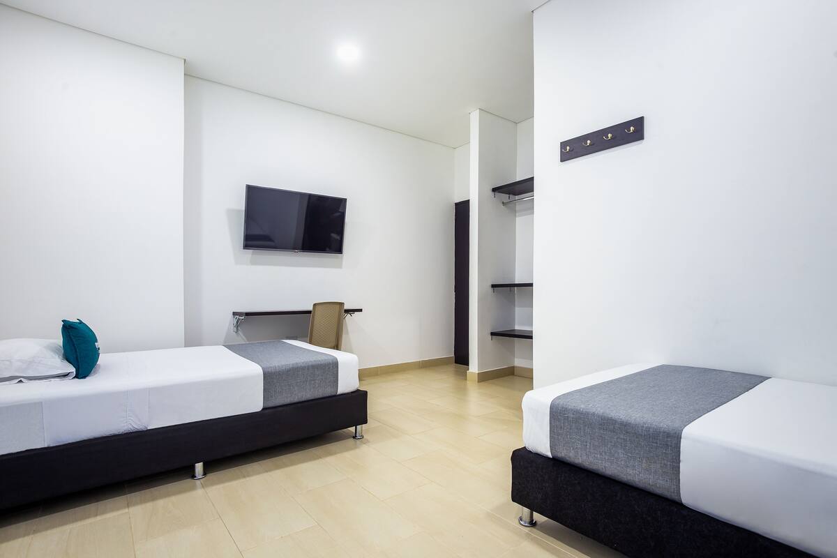 Ein modernes Hotelzimmer mit zwei Einzelbetten, einem flachbildfernseher an der Wand und einem Schrank mit Spiegel.
