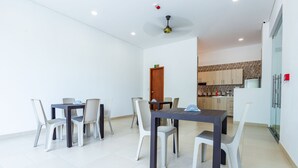 A modern dining area with a table and chairs, a kitchen in the background, and a ceiling fan.