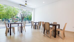 A modern dining area with multiple tables and chairs, large windows offering a view of the street, and a ceiling fan.