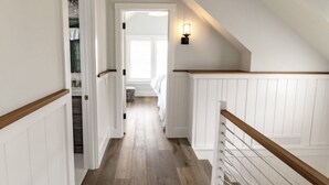 Un passadís estret amb terres de fusta i parets blanques, que condueix a una habitació amb finestra.