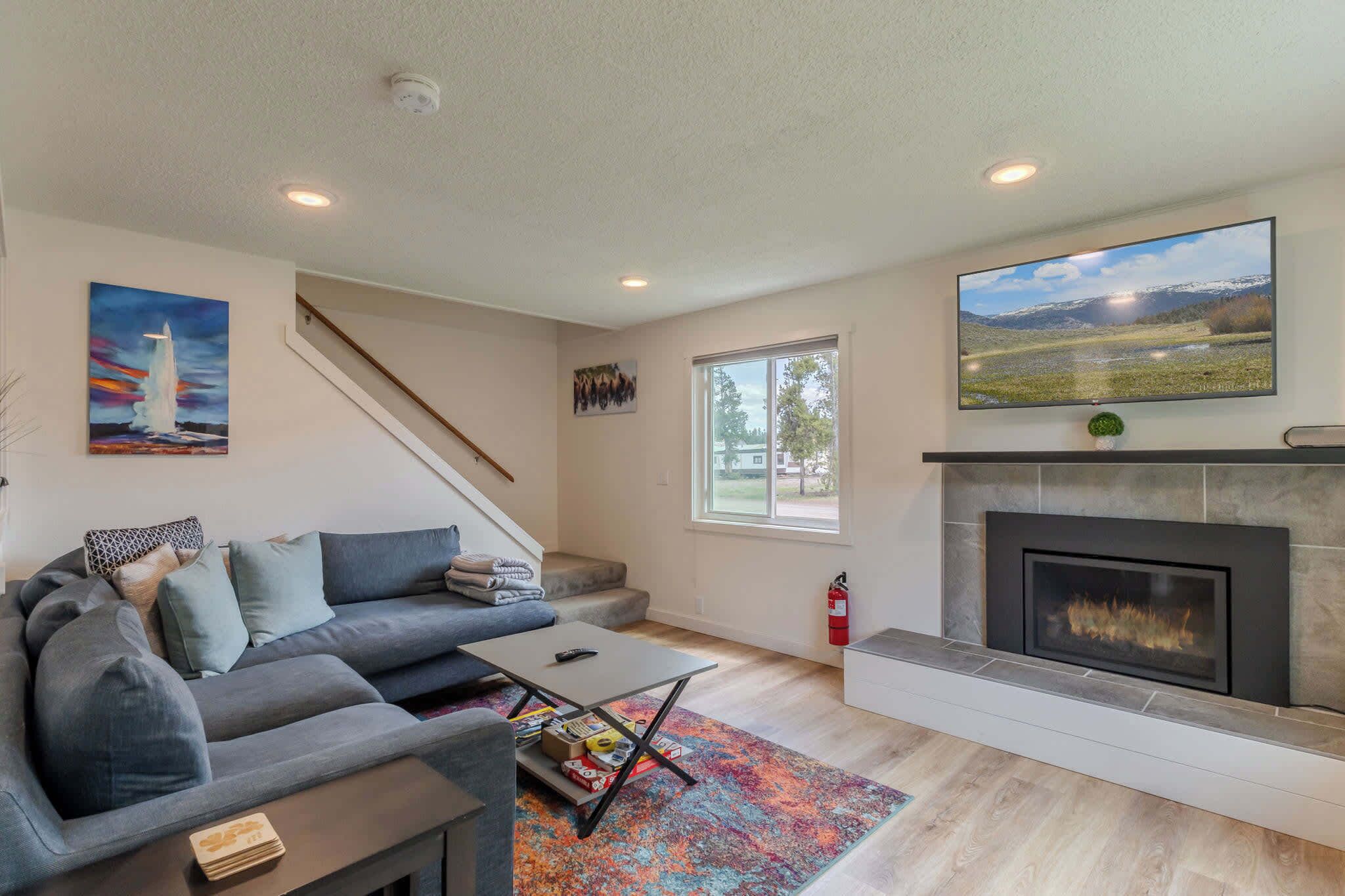 A modern living room with a gray sofa, a coffee table, a fireplace, and a large TV on the wall.