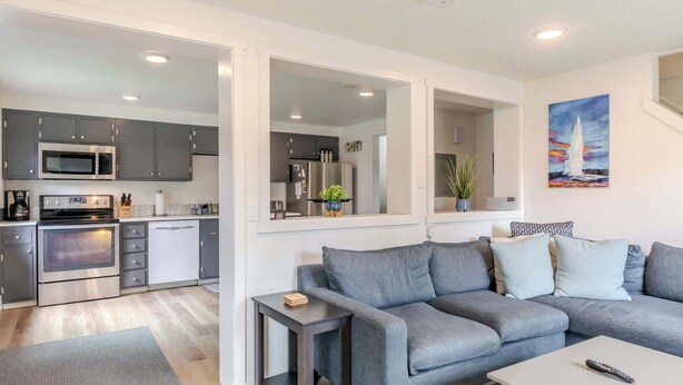 A modern kitchen with grey cabinets, stainless steel appliances, and a grey sofa in the living area.