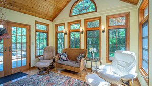 A spacious room with a high wooden ceiling, large windows with stained glass, a wicker sofa, a white leather chair, and a small round table with a vase of flowers. - Bright and peaceful Galena retreat. Near amenities and Chestnut (Galena)