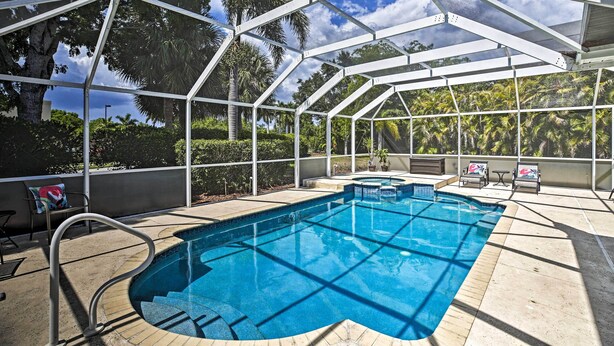 An indoor swimming pool with a glass ceiling, surrounded by lounge chairs and a view of palm trees. - Modern Beach Retreat w/ Pool, Hot Tub, & Patio! (Fort Myers)