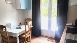 Eine Küche mit einem weißen Tisch, zwei Holzstühlen, einer Kaffeemaschine und einem Fenster mit Vorhängen.