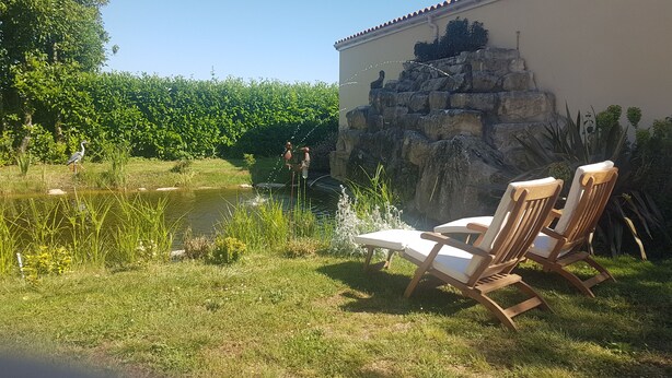 Ein Garten mit Teich, zwei Holzstühlen und einer Steinmauer.