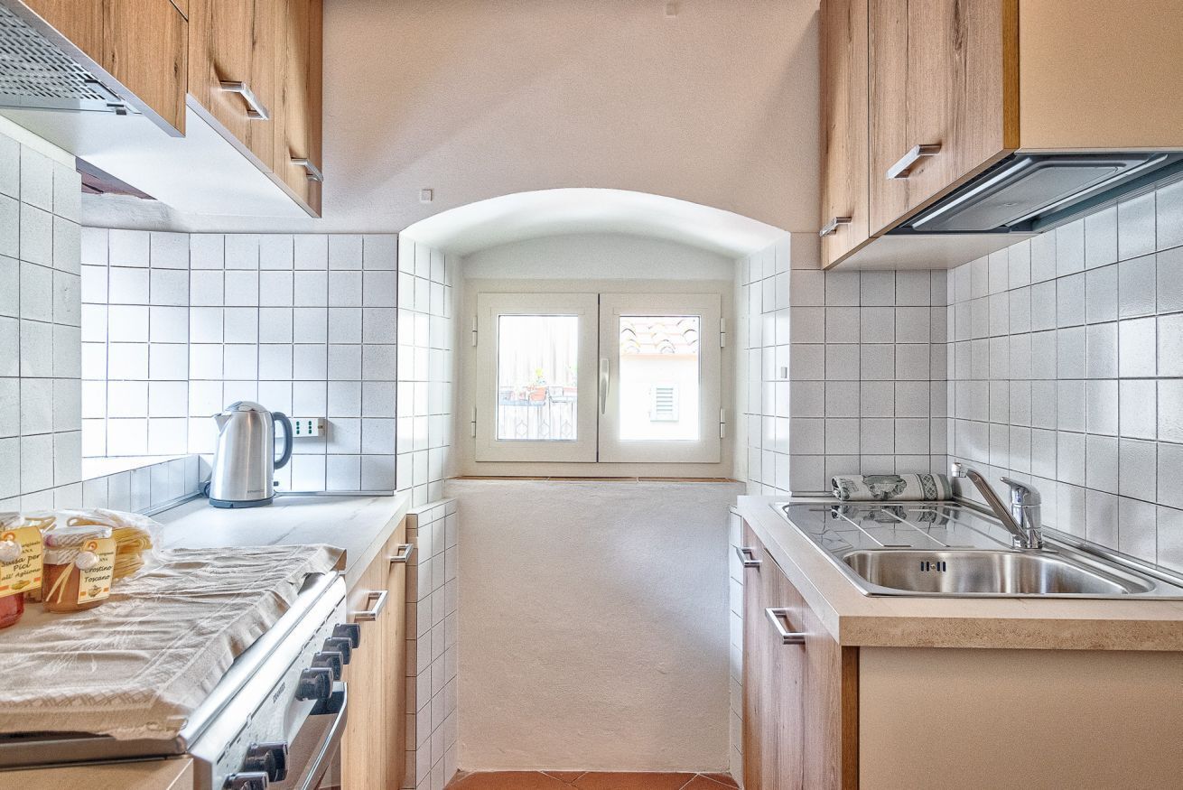 Una cucina con piastrelle bianche, mobili in legno, un lavello in acciaio inossidabile e una vista attraverso una porta.