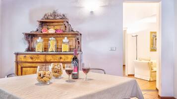 Un tavolo da pranzo con vasetti di vetro e bicchieri da vino, un mobiletto in legno con oggetti decorativi, e una porta che conduce in un'altra stanza.