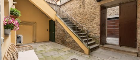 Un edificio de piedra con una escalera que lleva a un nivel superior, un banco y una puerta.
