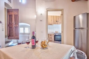 A dining area with a table set for two, a bottle of wine, and a bowl of snacks.