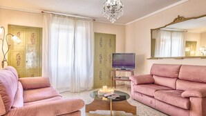 Een woonkamer met twee roze banken, een glazen salontafel, een televisie en een kroonluchter.