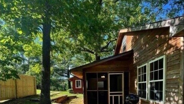 A wooden cabin with a porch, a barbecue grill, and a wooden fence in a wooded area. - The Hideaway at Bear Mountain Log Cabins (Eureka Springs)