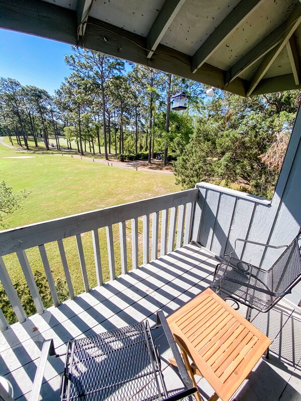A covered porch with a view of a golf course, a wooden table, and metal chairs.
