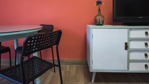 Een kamer met een witte kast, een zwarte televisie, een tafel en twee stoelen.
