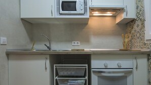 Een keuken met witte kastjes, een magnetron, een oven en een spoelbak.