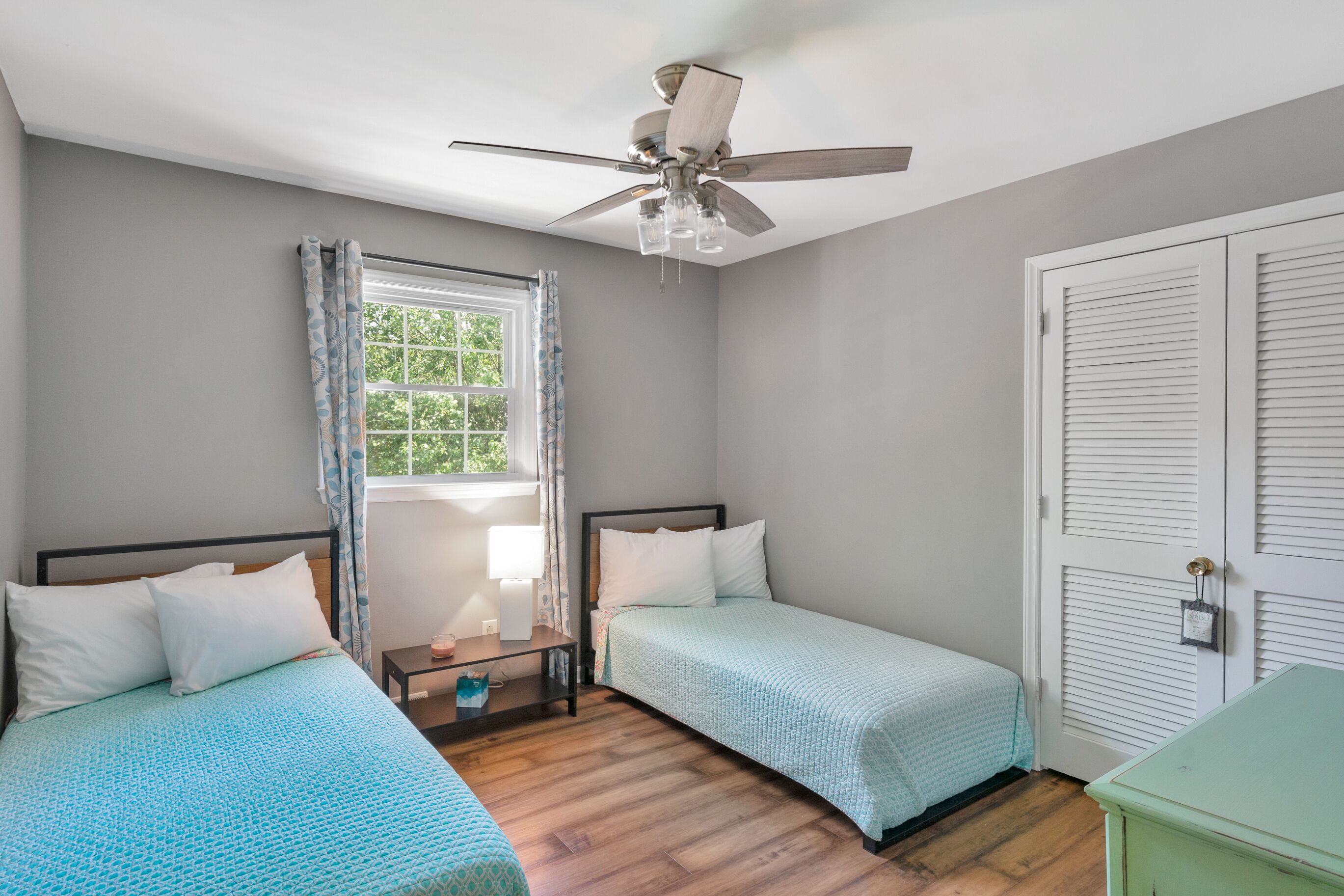 Un dormitorio con dos camas individuales, un ventilador de techo, una ventana con cortinas y una puerta con cerradura.